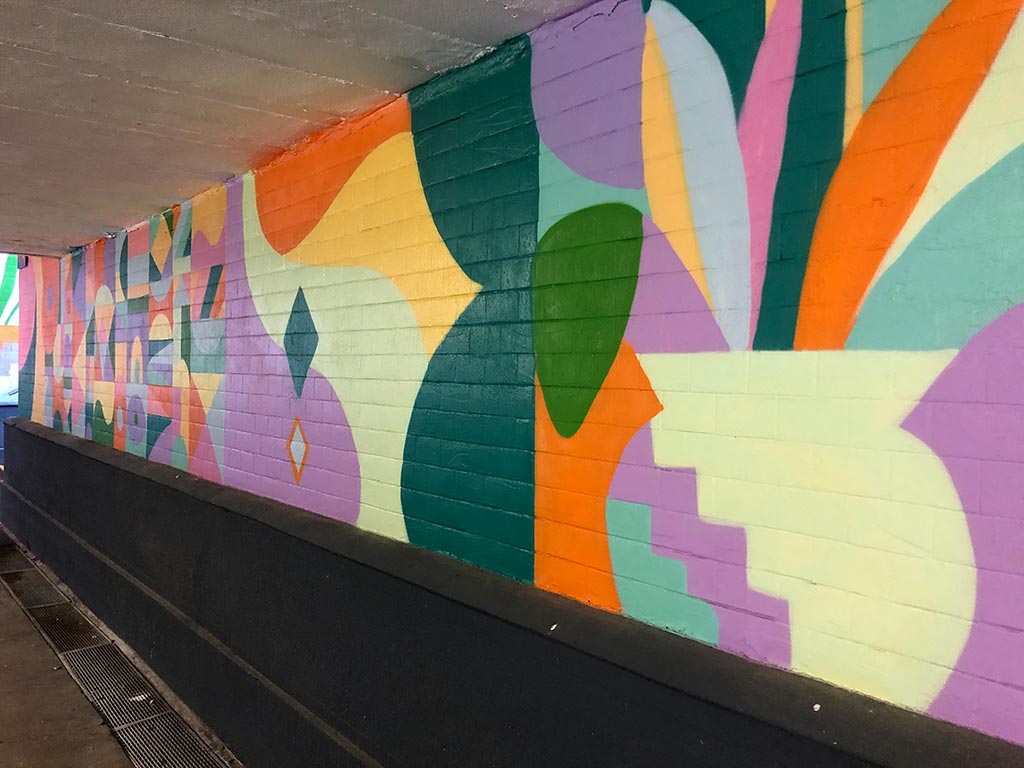 Mit bunten Formen und Pflanzen bemalte Unterführung am Bahnhof F-Mainkur